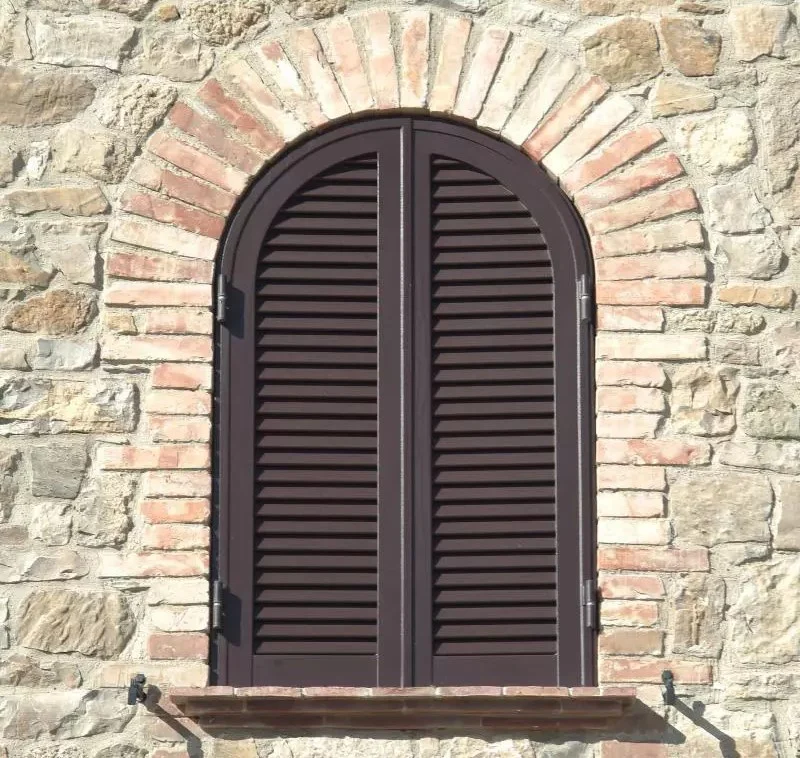 Finestra ad arco in muratura di pietra e mattoni con persiane scure chiuse (foto segnaposto del Figma)